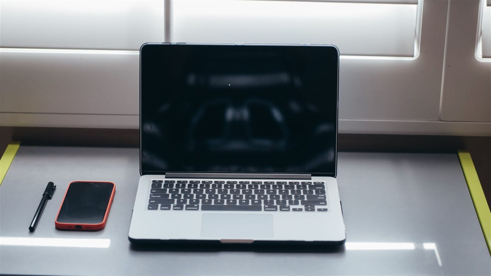 Smartphone beside a laptop and pen on a minimalist desk