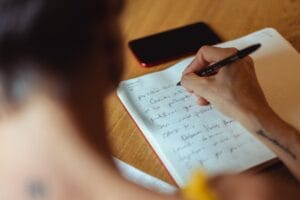 Person writing notes in a paper planner beside a face-down smartphone.
