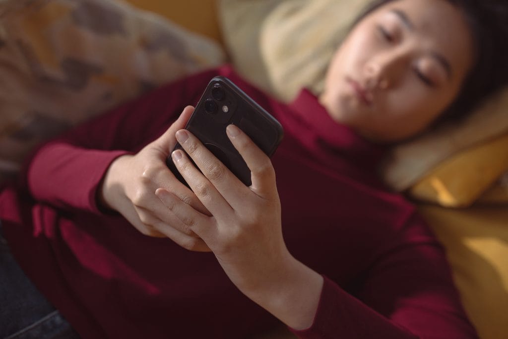 Person lying on a couch and looking at a smartphone held in both hands.