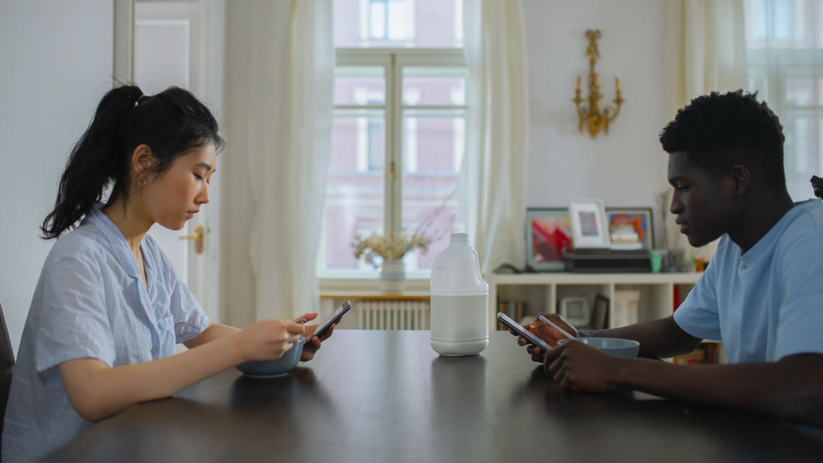 Couple looking at separate phones while sitting together at breakfast